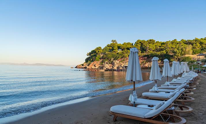 The Farewell Beach Day at a Greek beach club, sunbeds and umbrellas beside the Aegean sea